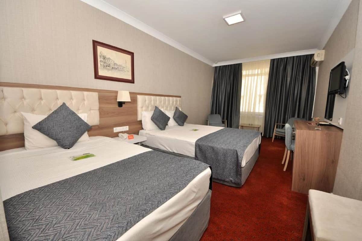 A hotel room with two beds, a desk, a chair, and a TV.