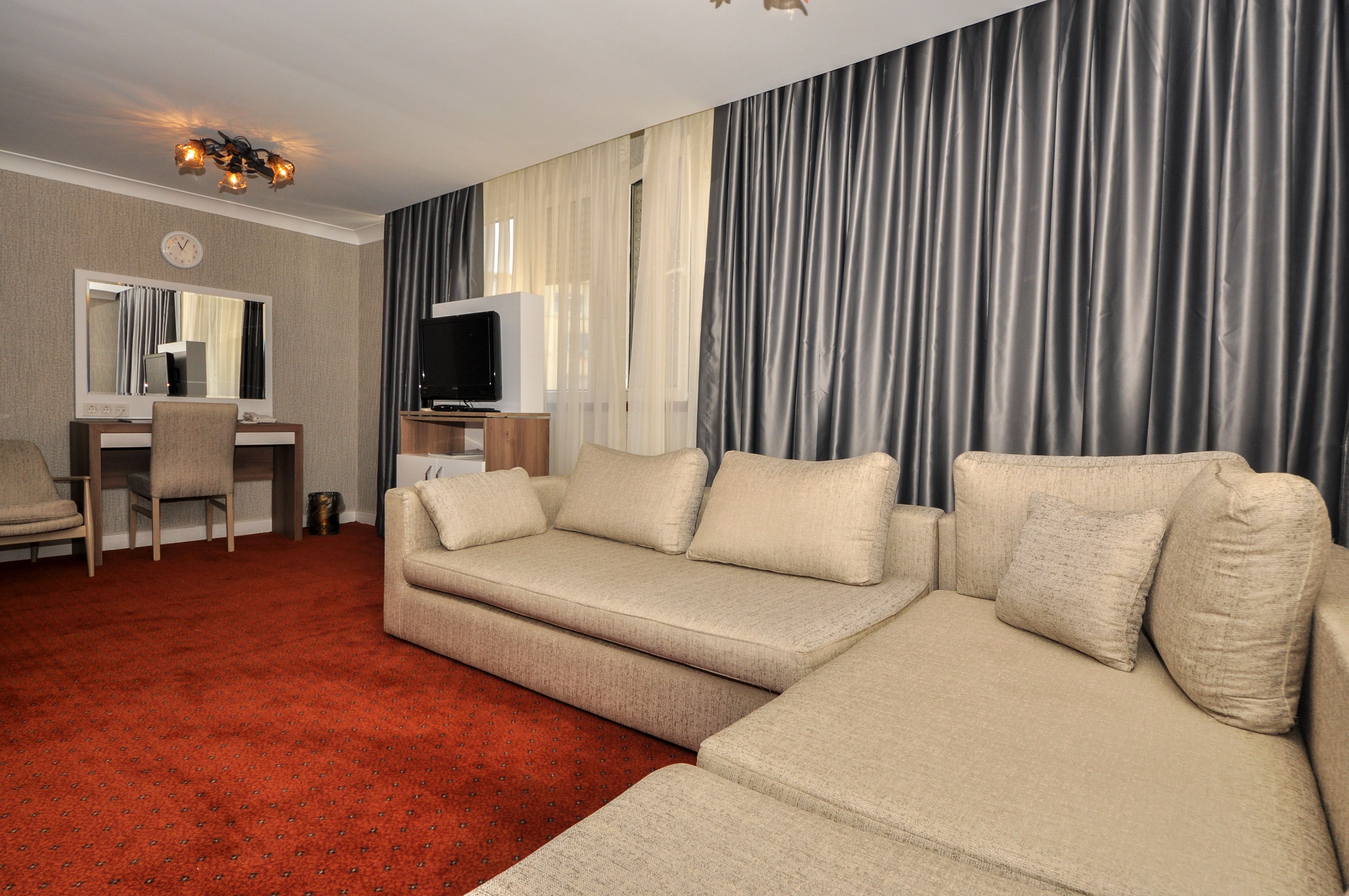 Una sala de estar con un sofá color beige, una alfombra roja, un televisor y un espejo.