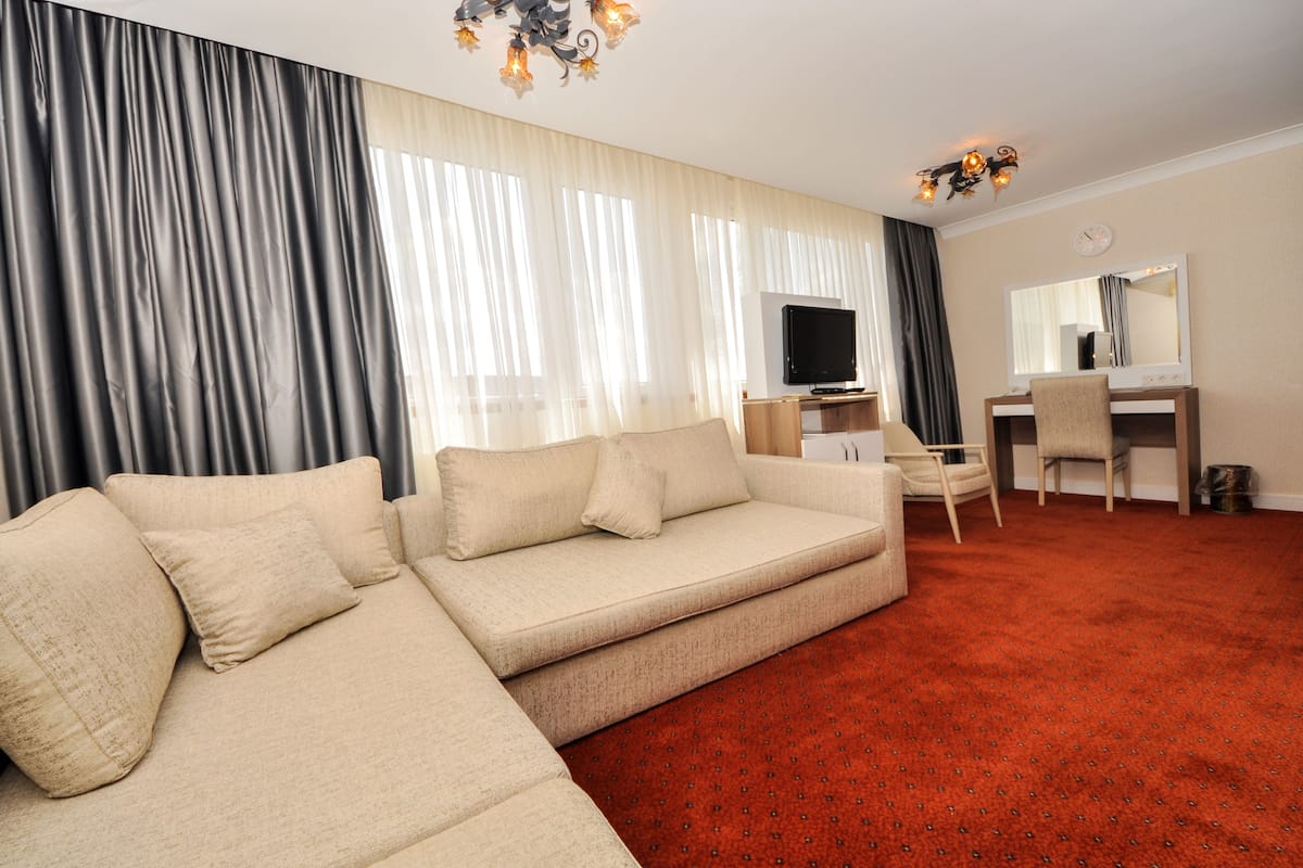 A living room with a beige sofa, a television, a desk with a chair, and a red carpet.