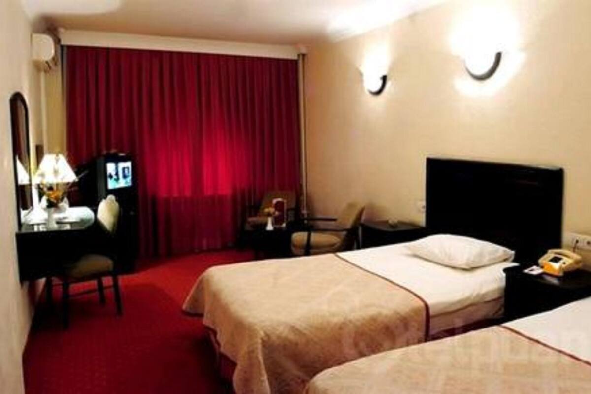 A hotel room with two beds, a desk with a lamp, a TV, and a red curtain.