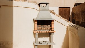 Ein gemauerter Grill für draußen mit Schornstein, ein Scherepaar und eine Holztür im Hintergrund.