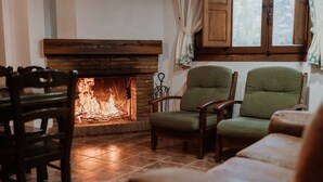 Ein gemütliches Wohnzimmer mit Kamin, Holzmöbeln und Blick ins Freie durch ein Fenster.