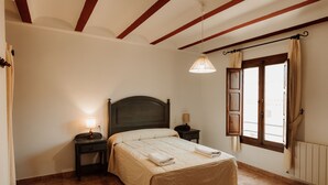 Ein Schlafzimmer mit Bett, Nachttischen, einer Hängelampe, einem Fenster mit Vorhängen und einer Heizung.