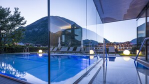 A swimming pool with clear glass walls, a view of mountains, and a poolside area with lounge chairs. - Hotel Auszeit (Eben am Achensee)