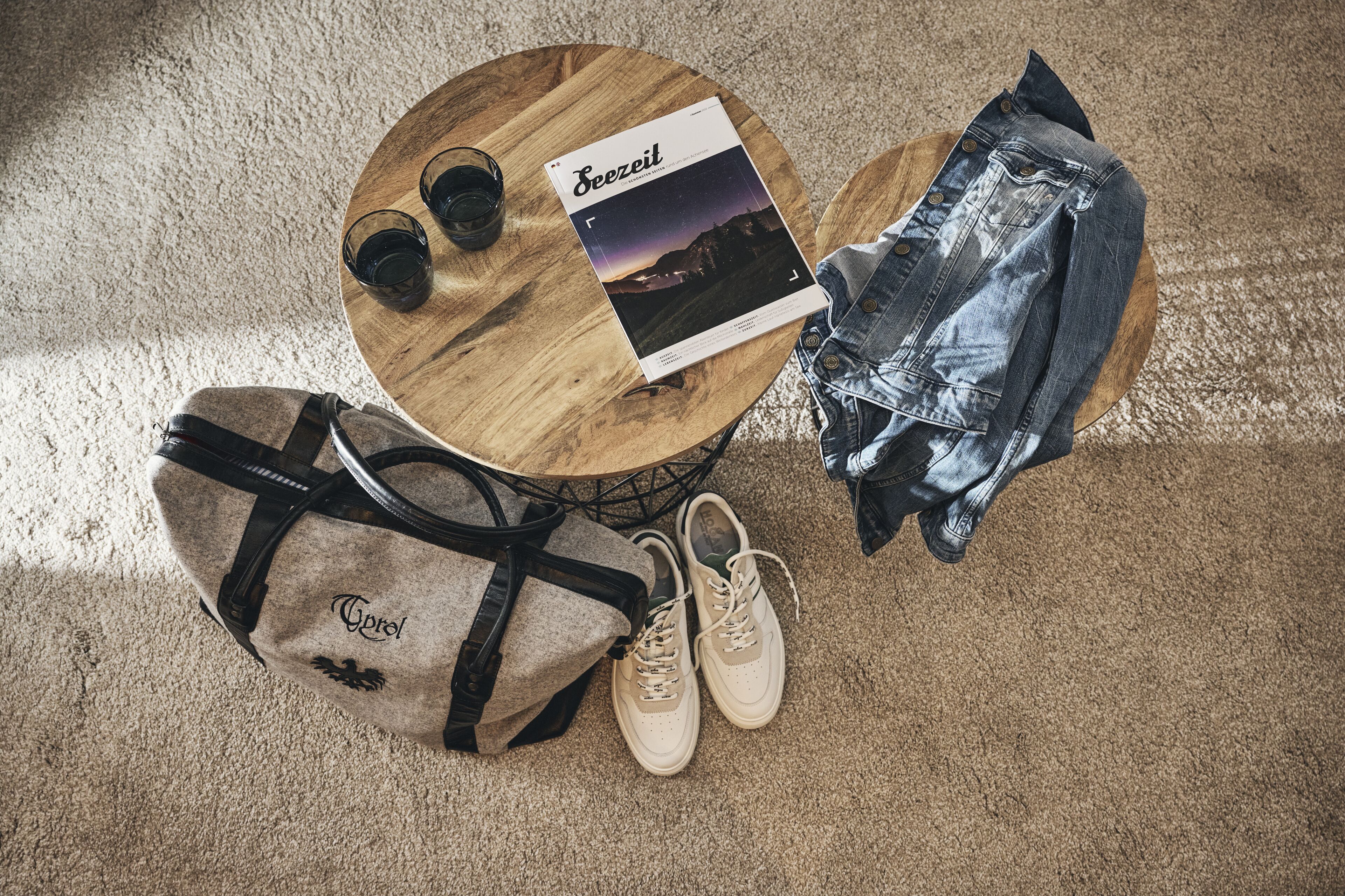 Une table ronde en bois, avec un magazine, une veste en jean, une paire de baskets et un sac.