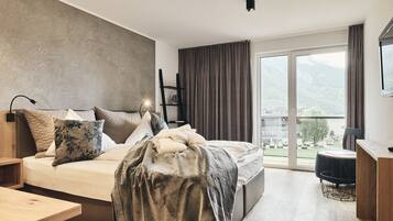 A modern bedroom with a large bed, a desk, and a view of mountains through the window.