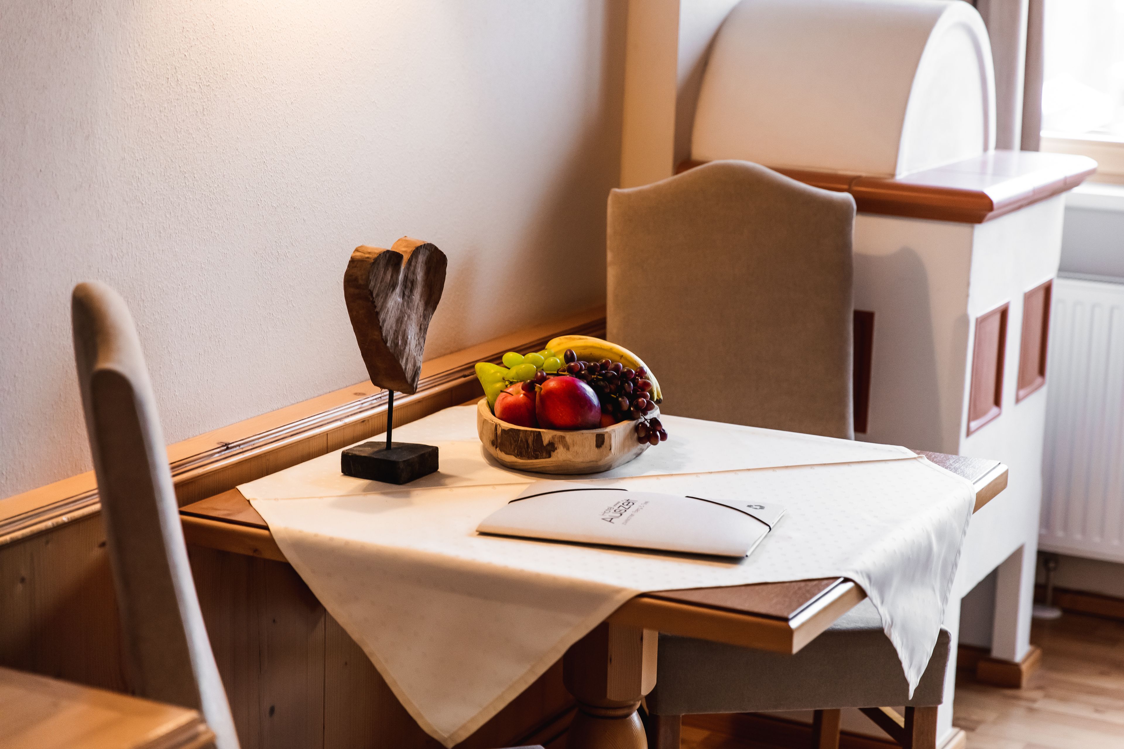 Una mesa de comedor con mantel blanco, un cuenco de fruta y una decoración con forma de corazón.