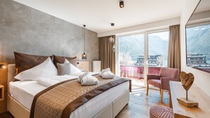 A modern hotel room with a large bed, a desk, and a view of mountains. - Hotel Auszeit (Eben am Achensee)