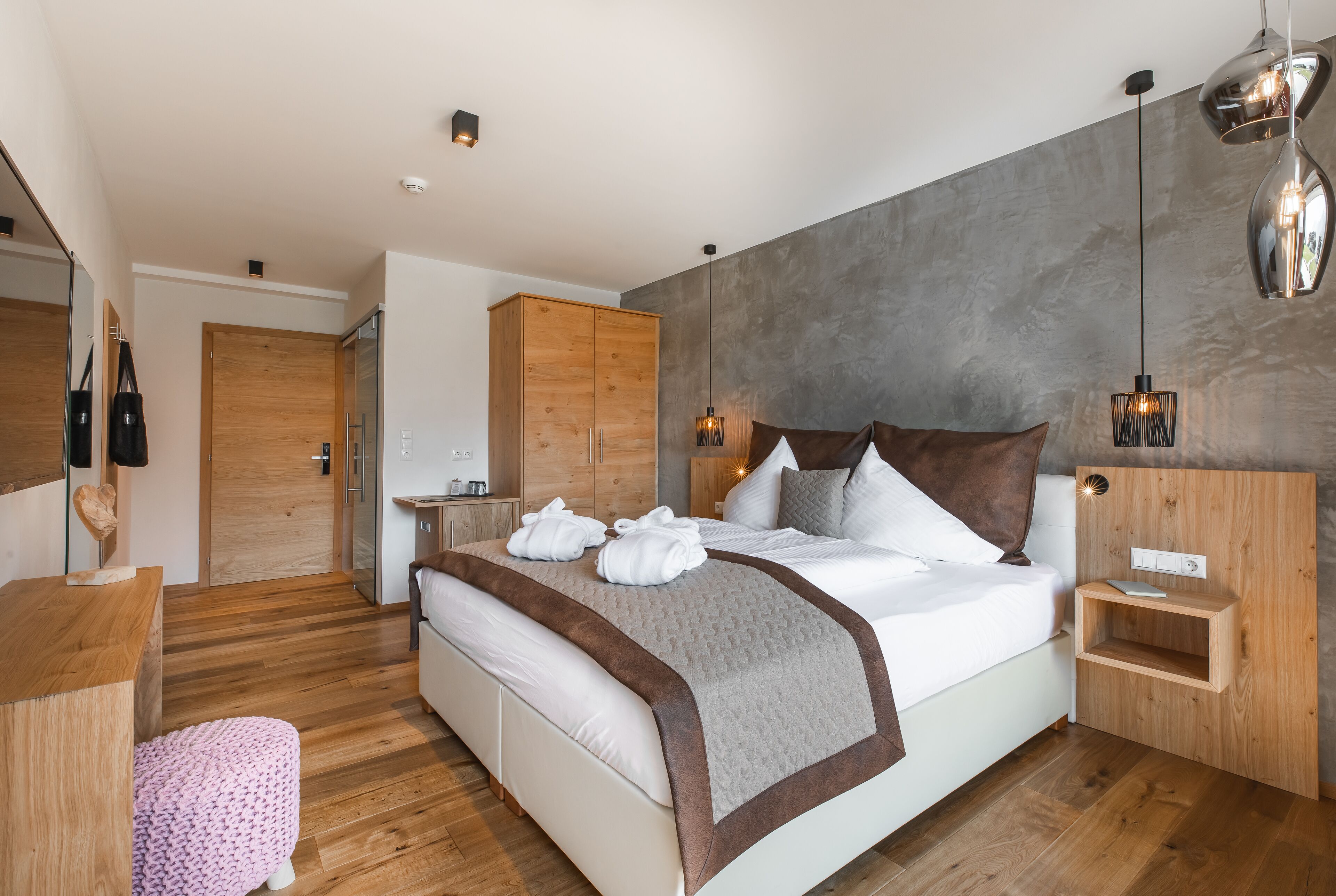 A modern bedroom with a large bed, wooden wardrobe, and a small bedside table.