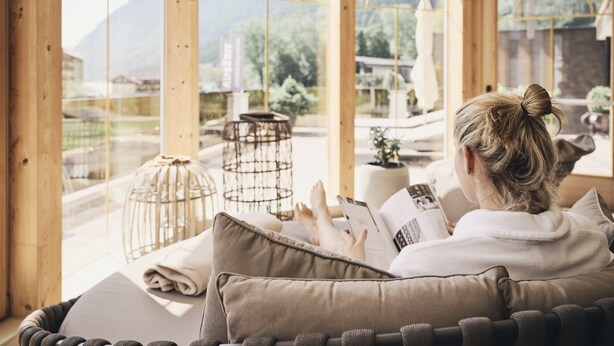 A person reading a book in a room with large windows, wooden beams, and a cozy seating area. - Hotel Auszeit (Eben am Achensee)