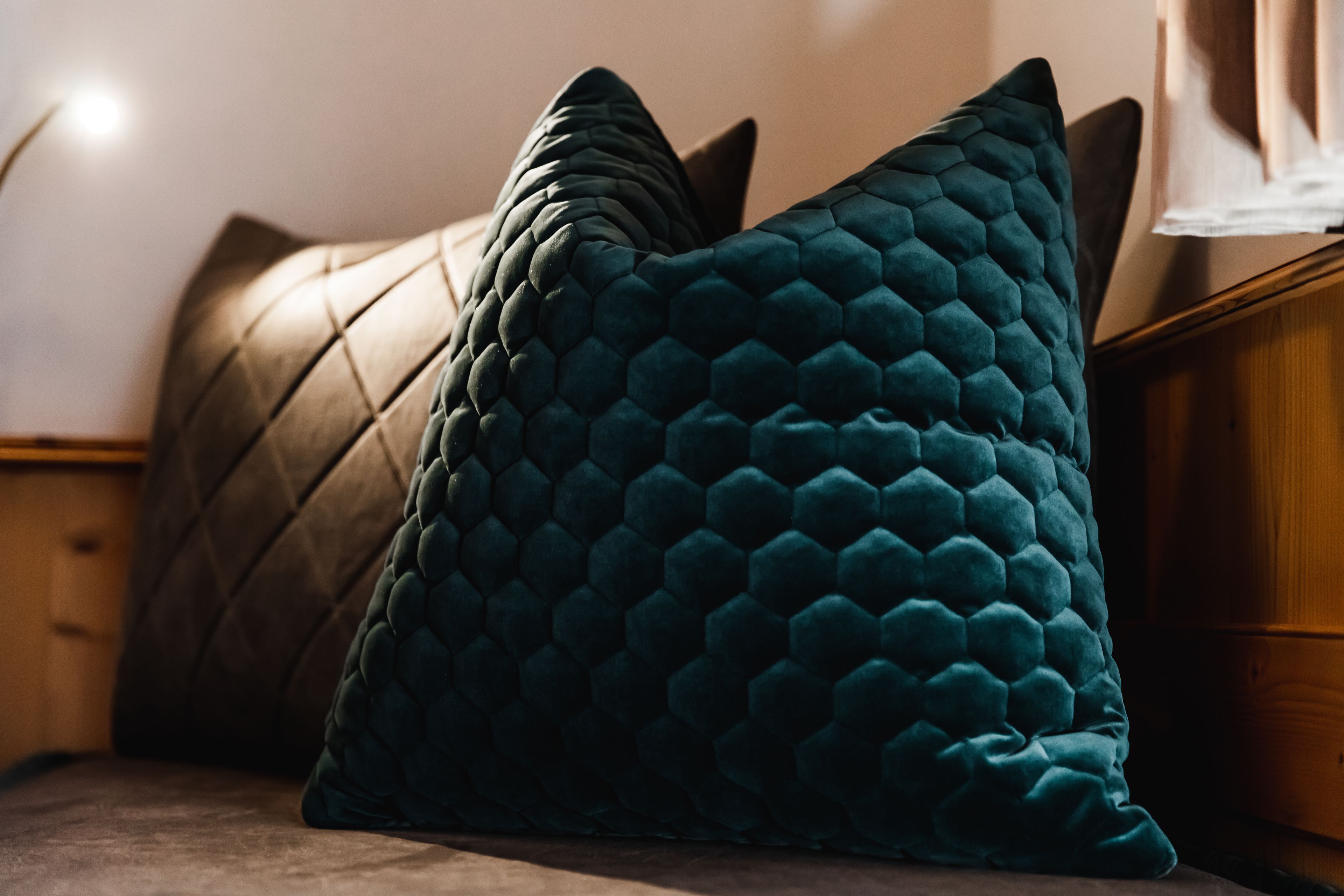 Una cama con dos almohadas, una verde azul oscuro y otra marrón.