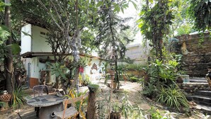 Un jardín con una mesa y sillas de piedra, rodeado de diversas plantas y un muro de piedra.