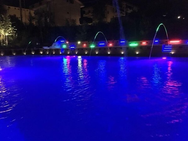 A nighttime view of a water feature with illuminated arches reflecting on the water.