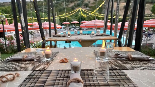 A dining table set with candles, glasses, and napkins, overlooking a pool area with umbrellas.