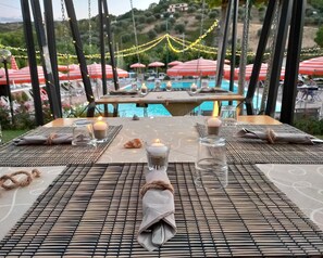 A dining table set with candles, glasses, and napkins, overlooking a pool area with umbrellas.