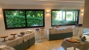 A buffet setup with various food items on tables, large windows with greenery outside, and a clean, modern interior.