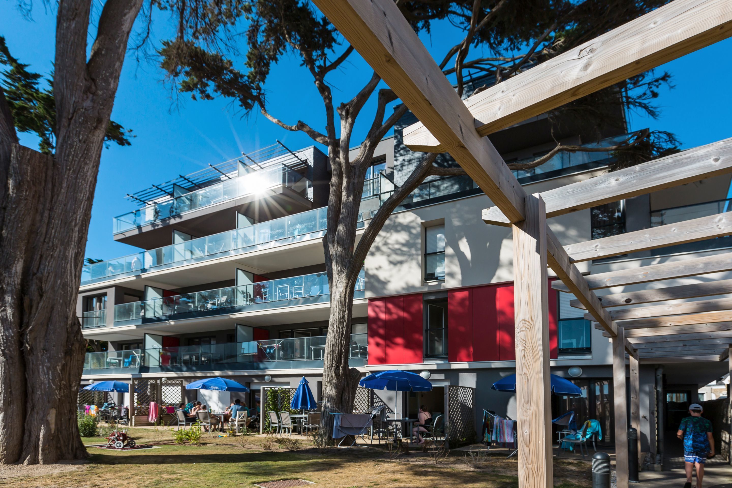 A multi-story building with outdoor seating and umbrellas, surrounded by trees.