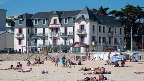 A beachfront hotel with multiple balconies, a sandy beach in front, and a clear blue sky. - Résidence Odalys de La Plage (Pornichet)