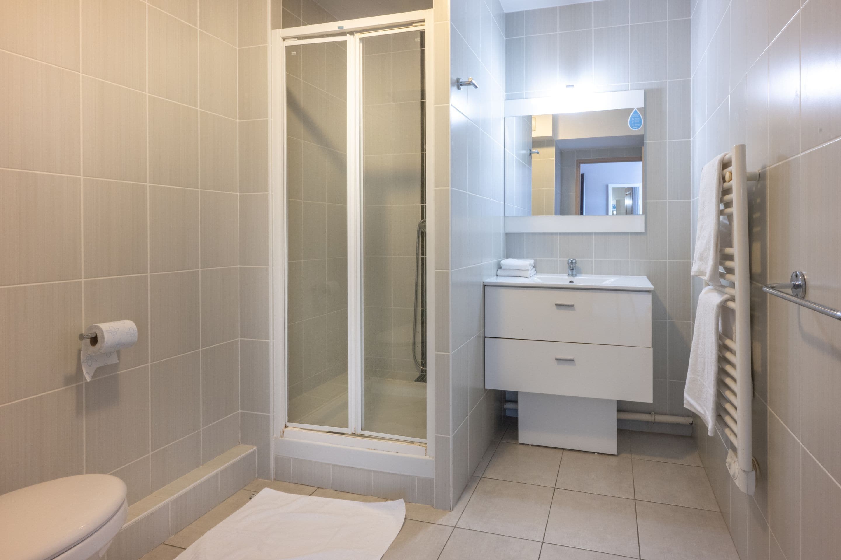 A modern bathroom with a glass-enclosed shower, a toilet, a sink with a mirror, and a towel rack.