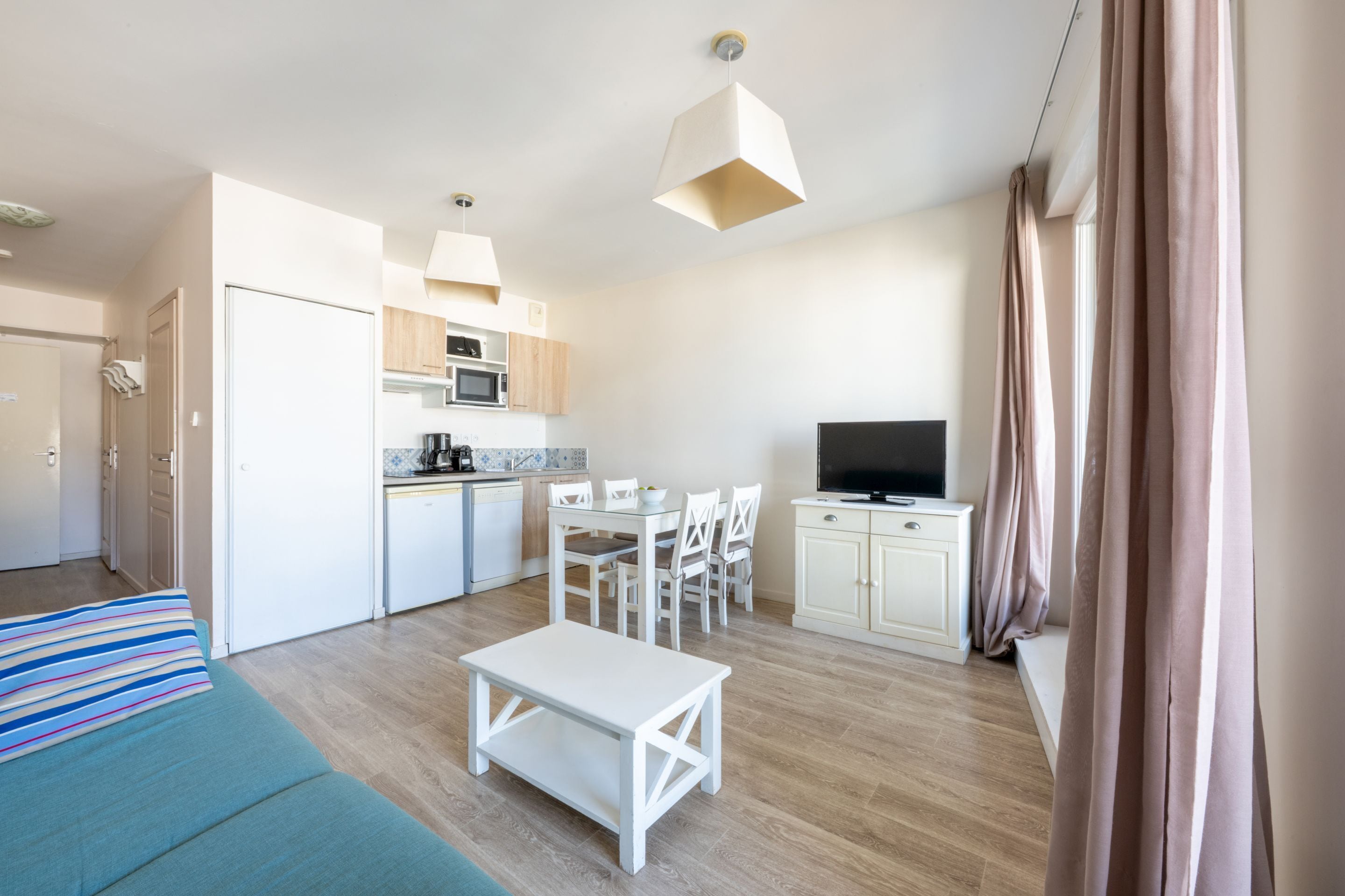 Ein moderner, gut beleuchteter Raum mit einer Küchenzeile, einem Essbereich, einem Fernseher und einem Bett.