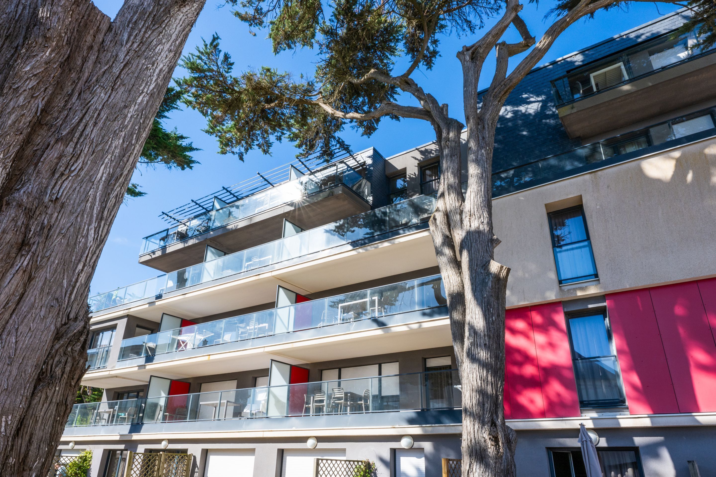Un immeuble à plusieurs étages, doté de balcons, de grandes fenêtres et d’un arbre au premier plan.