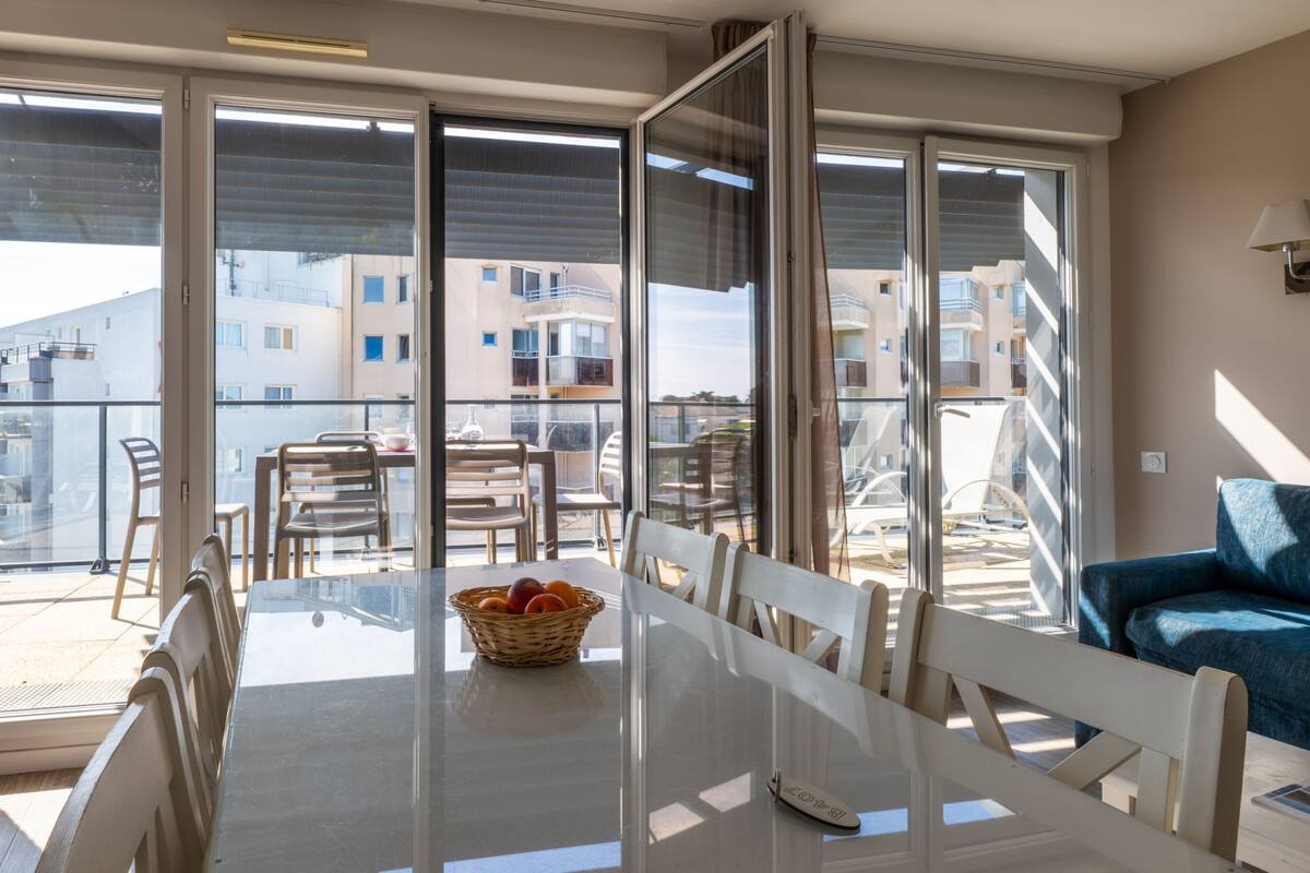A dining area with a glass table, chairs, and a basket of fruit.