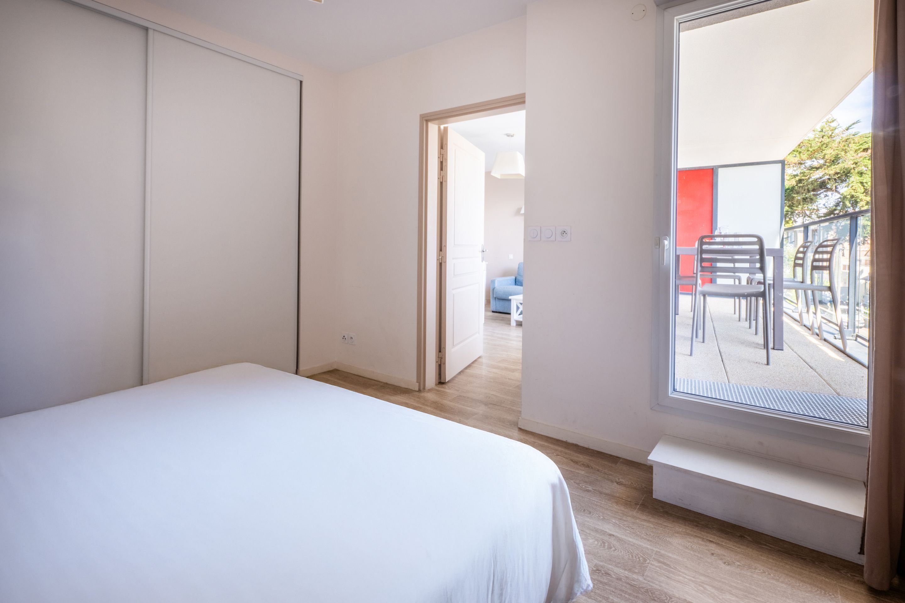 A bedroom with a large bed, a sliding door, and a balcony with chairs.