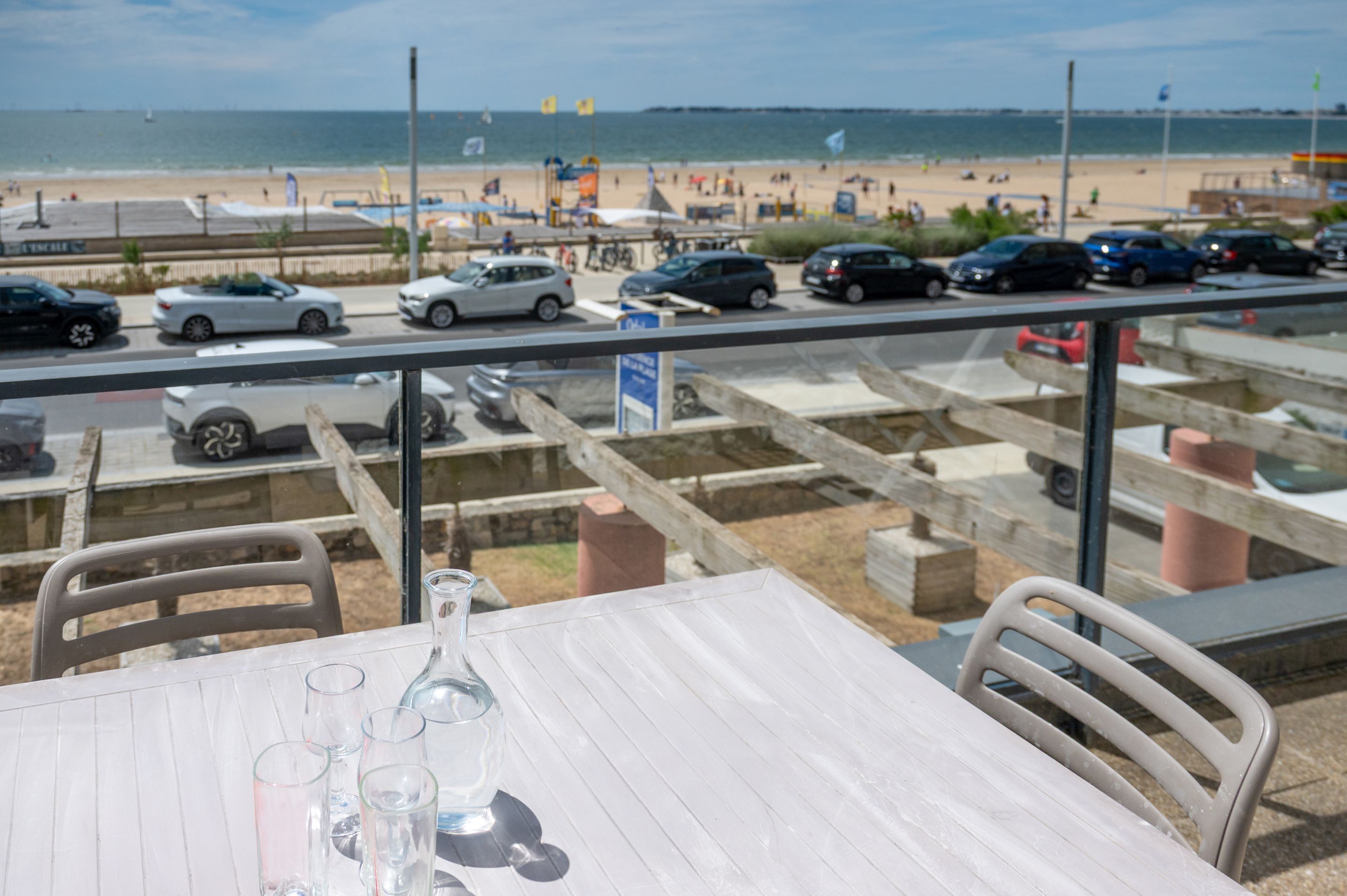 A table with chairs and a view of a beach and parking area.
