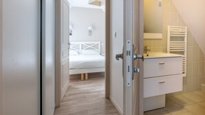 A bedroom with a bed, a bedside table, and a bathroom with a sink and towel rack. - Résidence Odalys de La Plage (Pornichet)