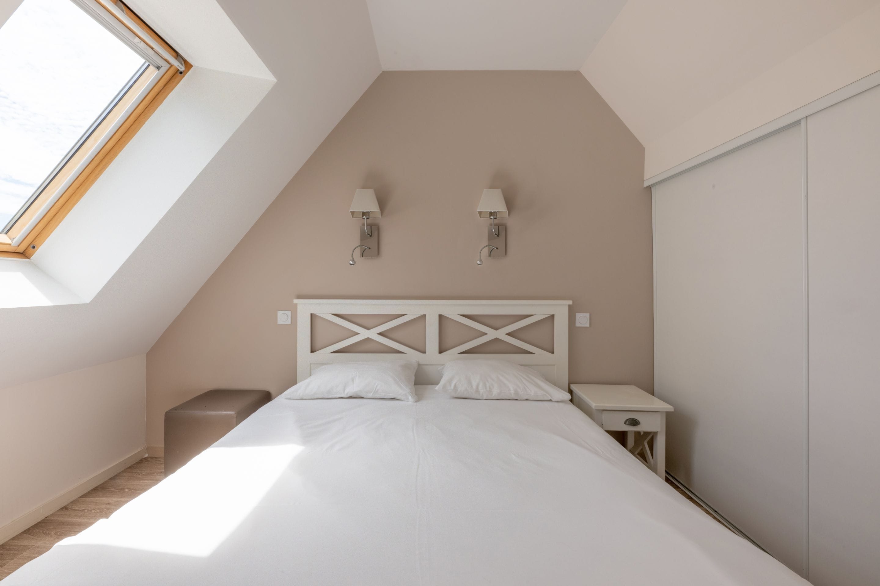 Ein Schlafzimmer mit schrägem Dach, einem Bett mit weißer Bettwäsche, zwei Nachttischen und Wandleuchten.