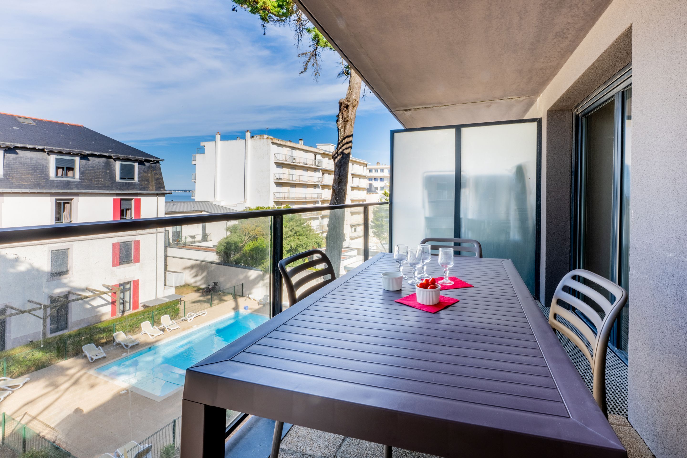 A balcony with a table set for two, overlooking a swimming pool and buildings.