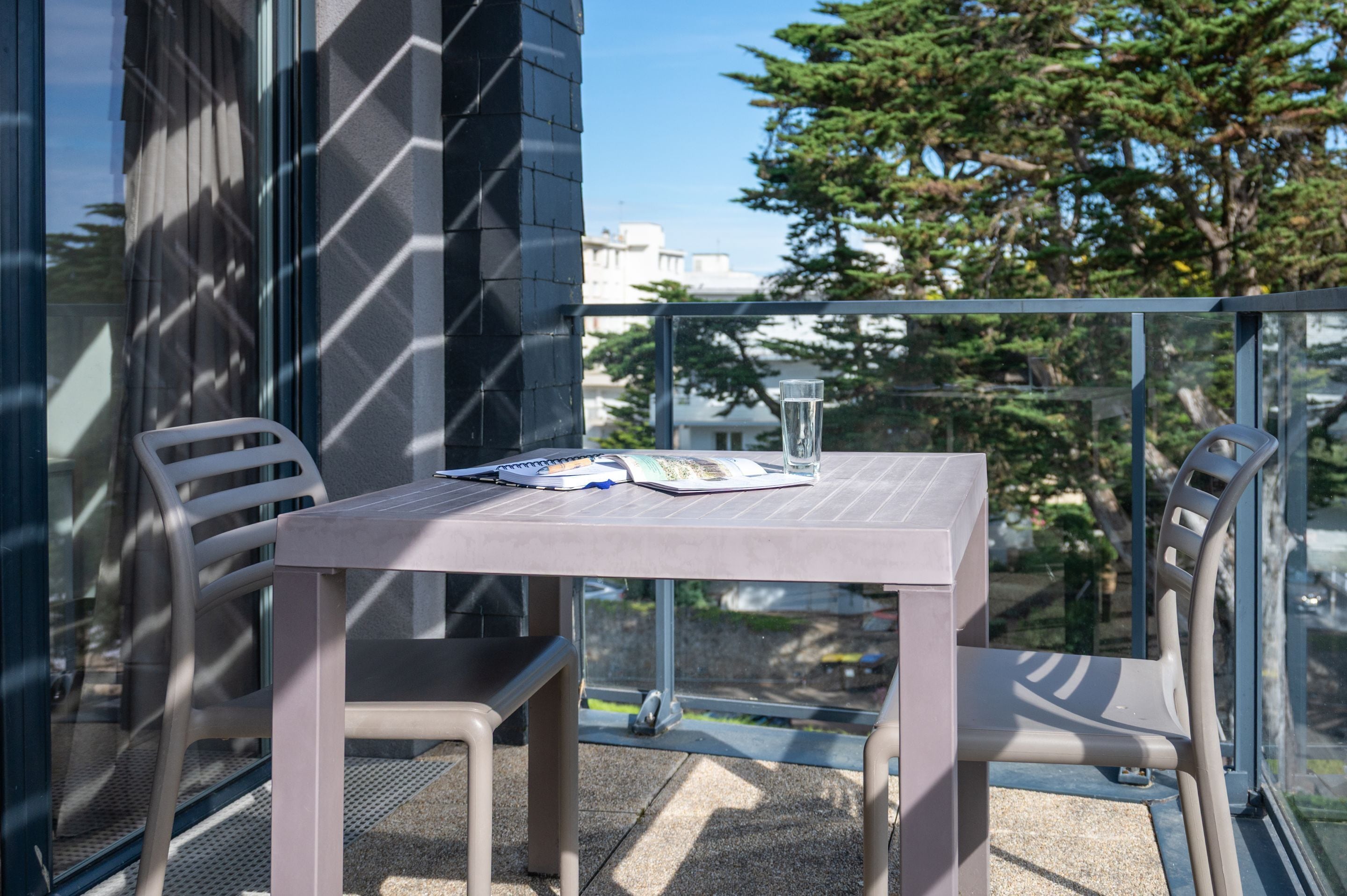 A balcony with a table and chairs, a glass of water, and a book.