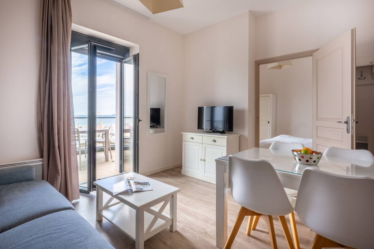 A modern hotel room with a balcony, a dining area, a TV, and a white cabinet.