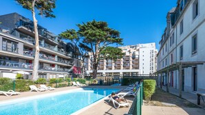 A swimming pool area with lounge chairs, a pergola, and multi-story buildings in the background. - Résidence Odalys de La Plage (Pornichet)