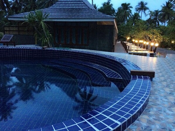 A swimming pool with blue tiles, a small building with a tiled roof, and palm trees in the background. - Ruean Thai Nai Bang by Pansak Resort (Surat Thani)