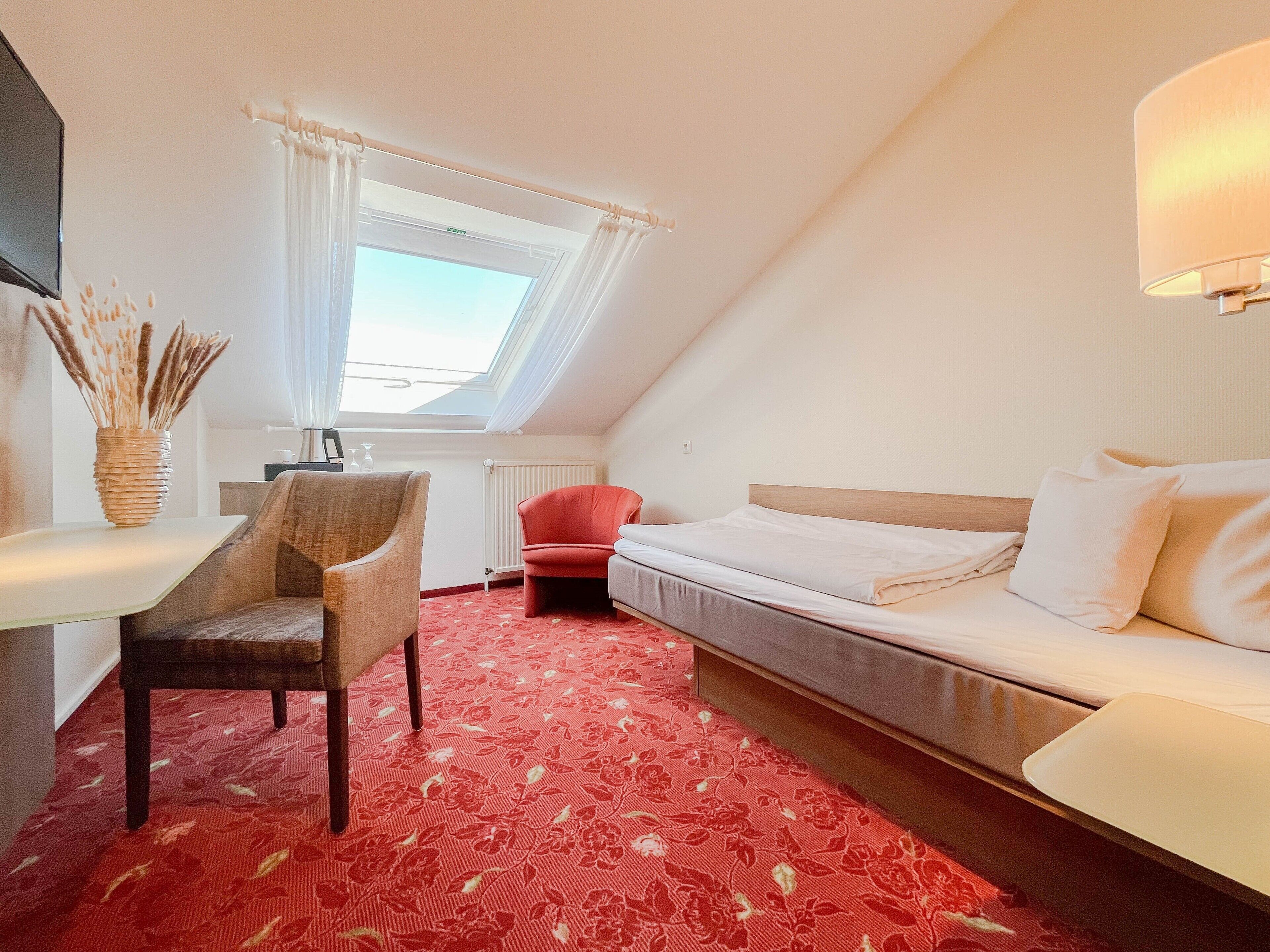 A room with a bed, a desk, a chair, a window with curtains, and a radiator.