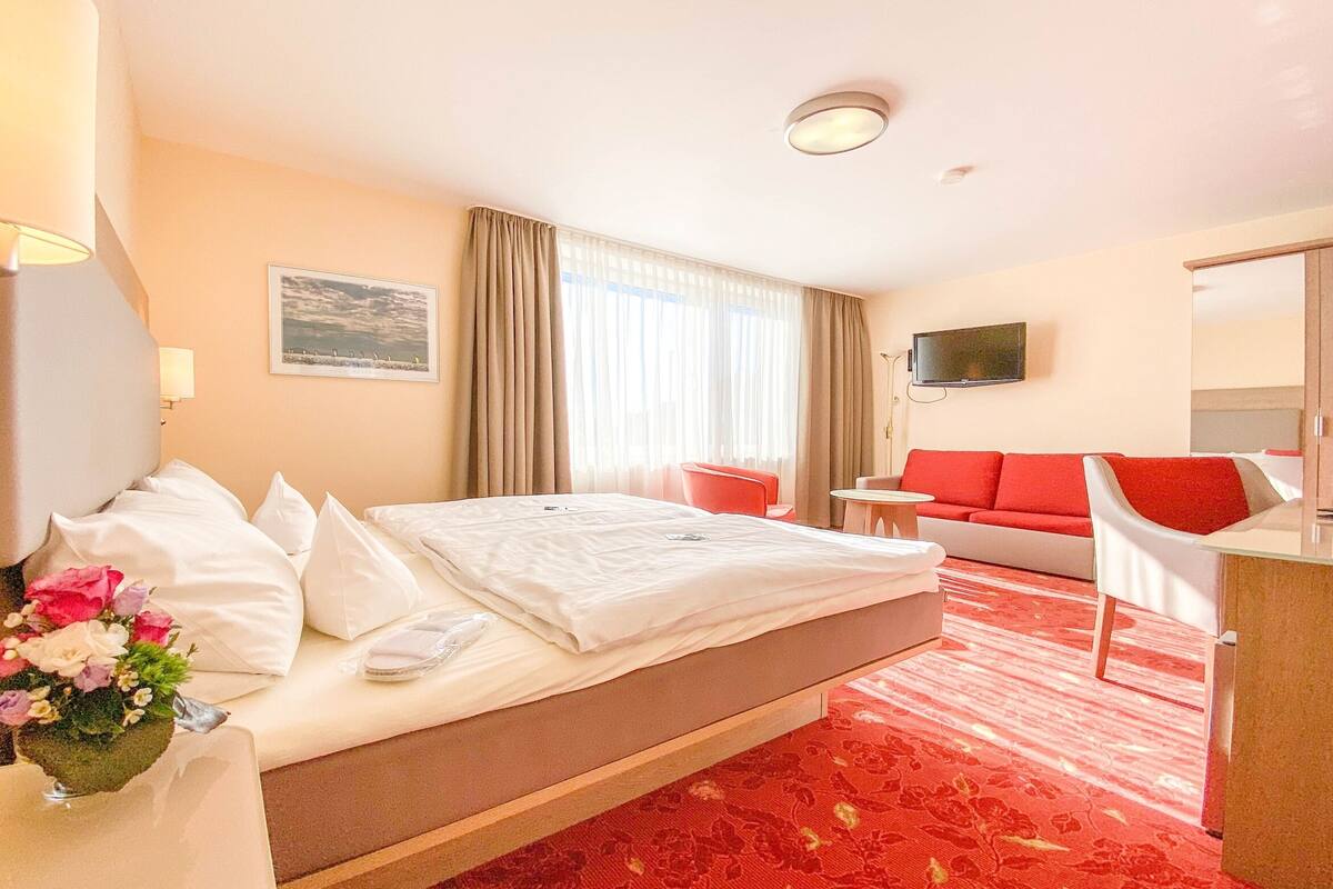 A hotel room with a bed, a desk, a chair, a TV, and a window with curtains.