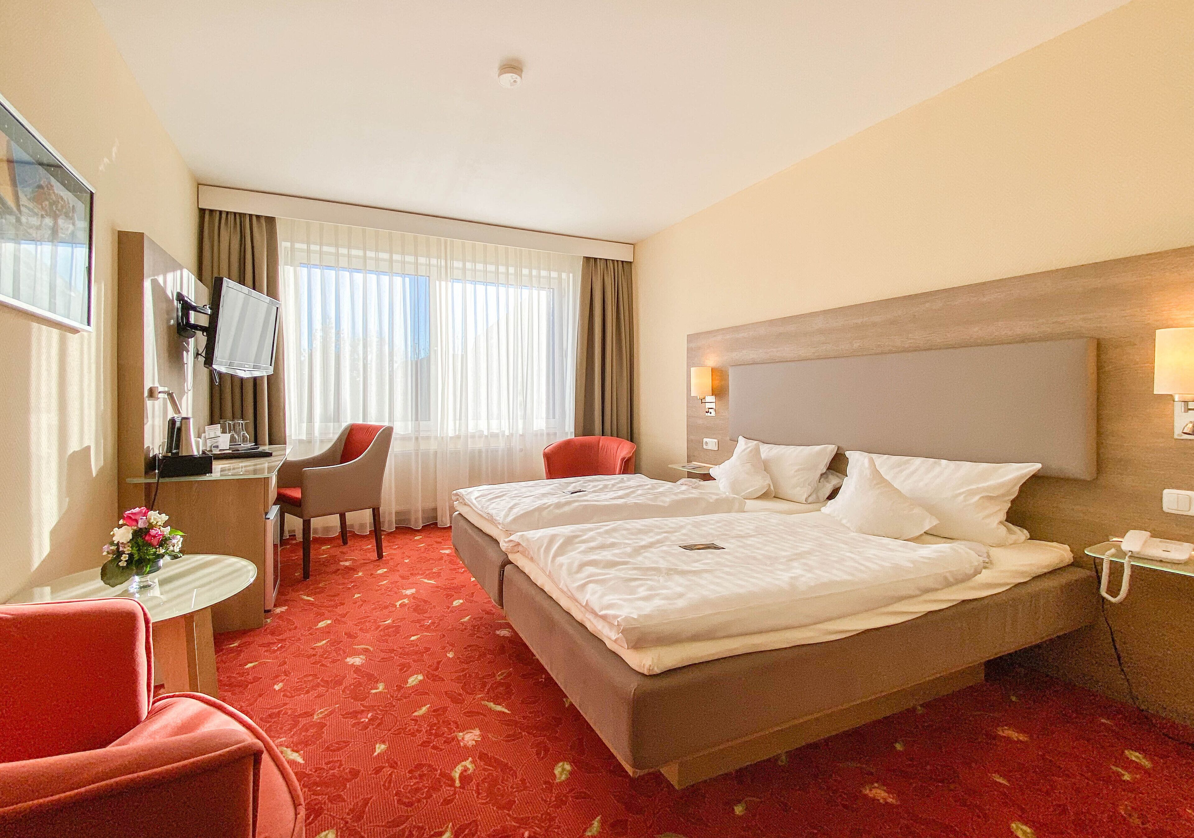 Quarto de hotel com duas camas, uma escrivaninha, uma cadeira, uma televisão e uma janela com cortinas.