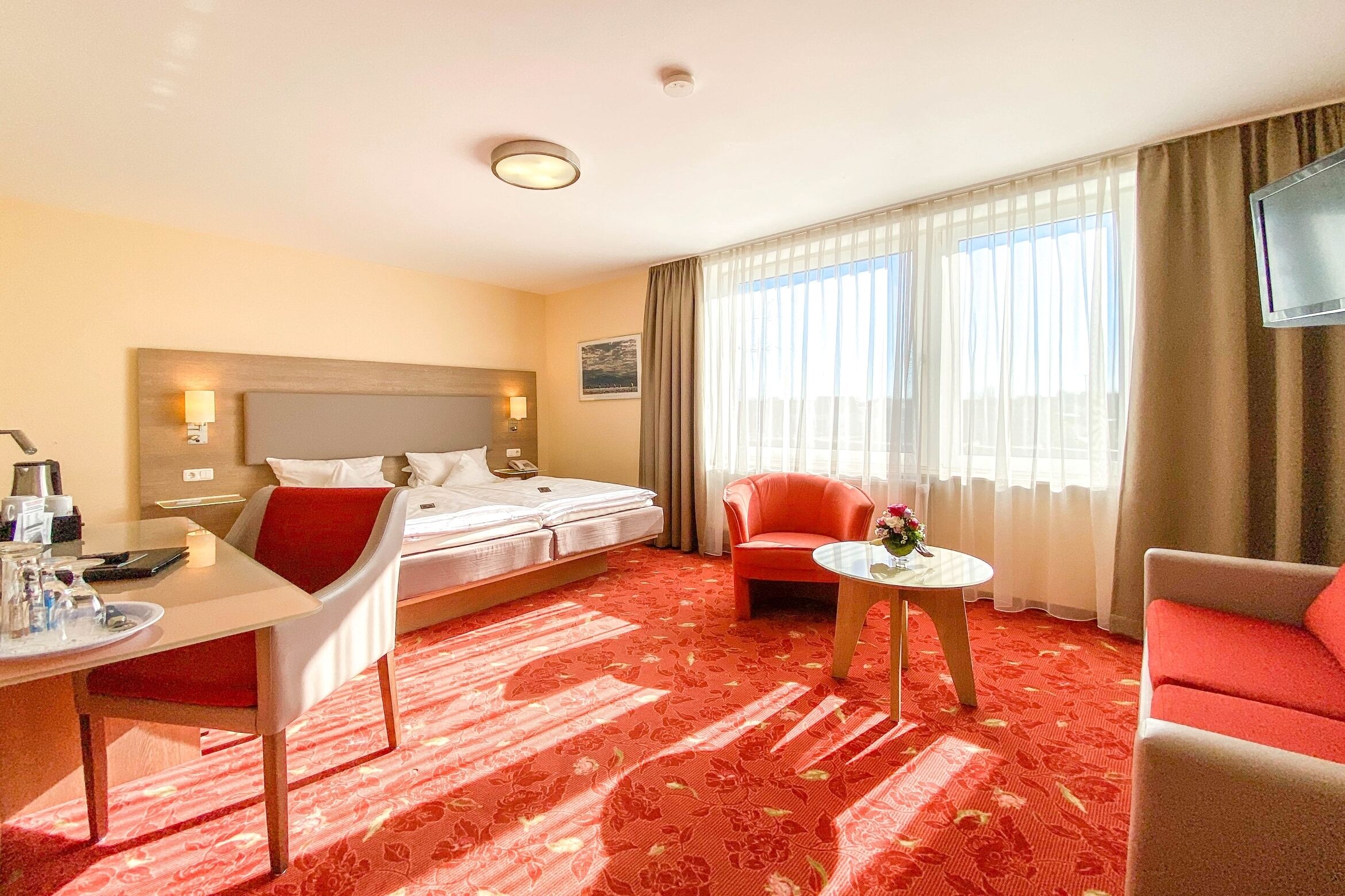 Ein Hotelzimmer mit Bett, Schreibtisch, Stuhl, Sofa, einem kleinen Tisch und Fernseher.