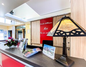 A reception desk with a lamp, magazines, and a red wall with a welcome message. - Vier Linden Kiek In Hotel (Stade)