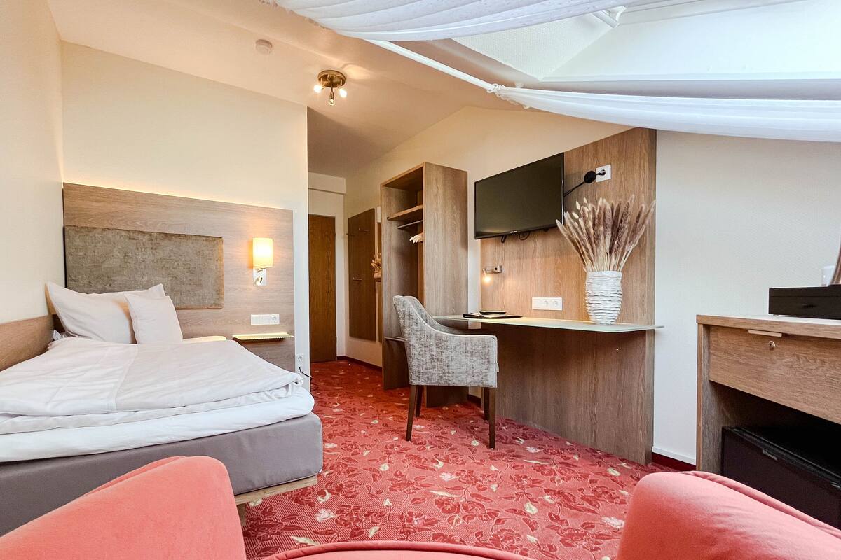 A hotel room with a bed, a desk, a chair, a TV, and a decorative vase.