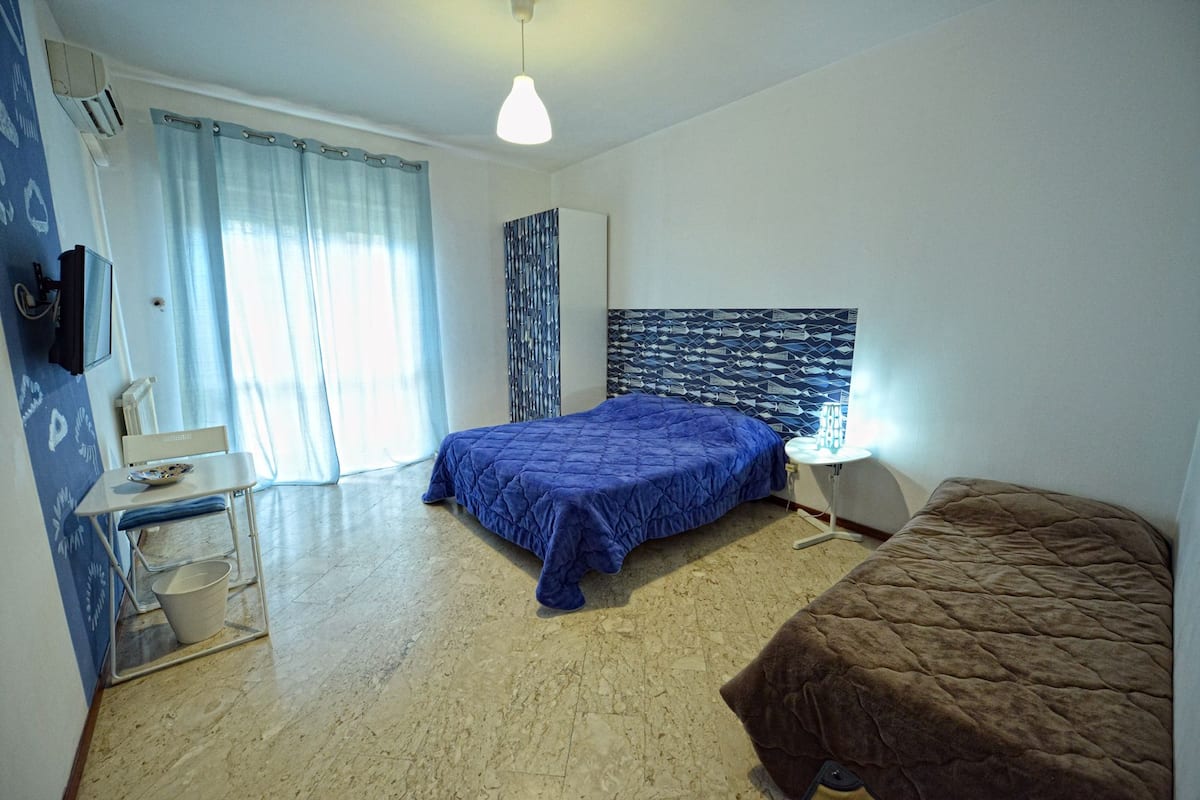 A bedroom with a bed, a bedside table, a lamp, a chair, and a window with curtains.