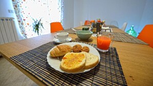 Desayuno con croissants, muffins, tostadas, una taza de café, un bol y un vaso de jugo de naranja sobre una mesa.