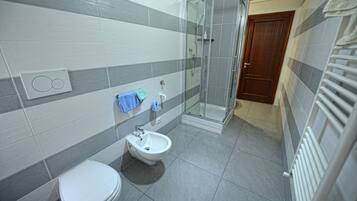 A bathroom with a toilet, bidet, and glass-enclosed shower.