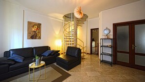 Una sala de estar con un sofá de cuero negro, una pequeña mesa redonda, una escalera de caracol y una puerta de madera.