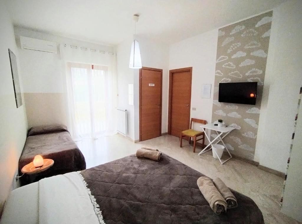 Habitación de hotel con dos camas, un televisor montado en la pared, una mesita y una silla.