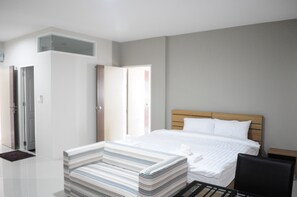 A modern hotel room with a large bed, a striped sofa, a wooden nightstand, and a door leading to another room.