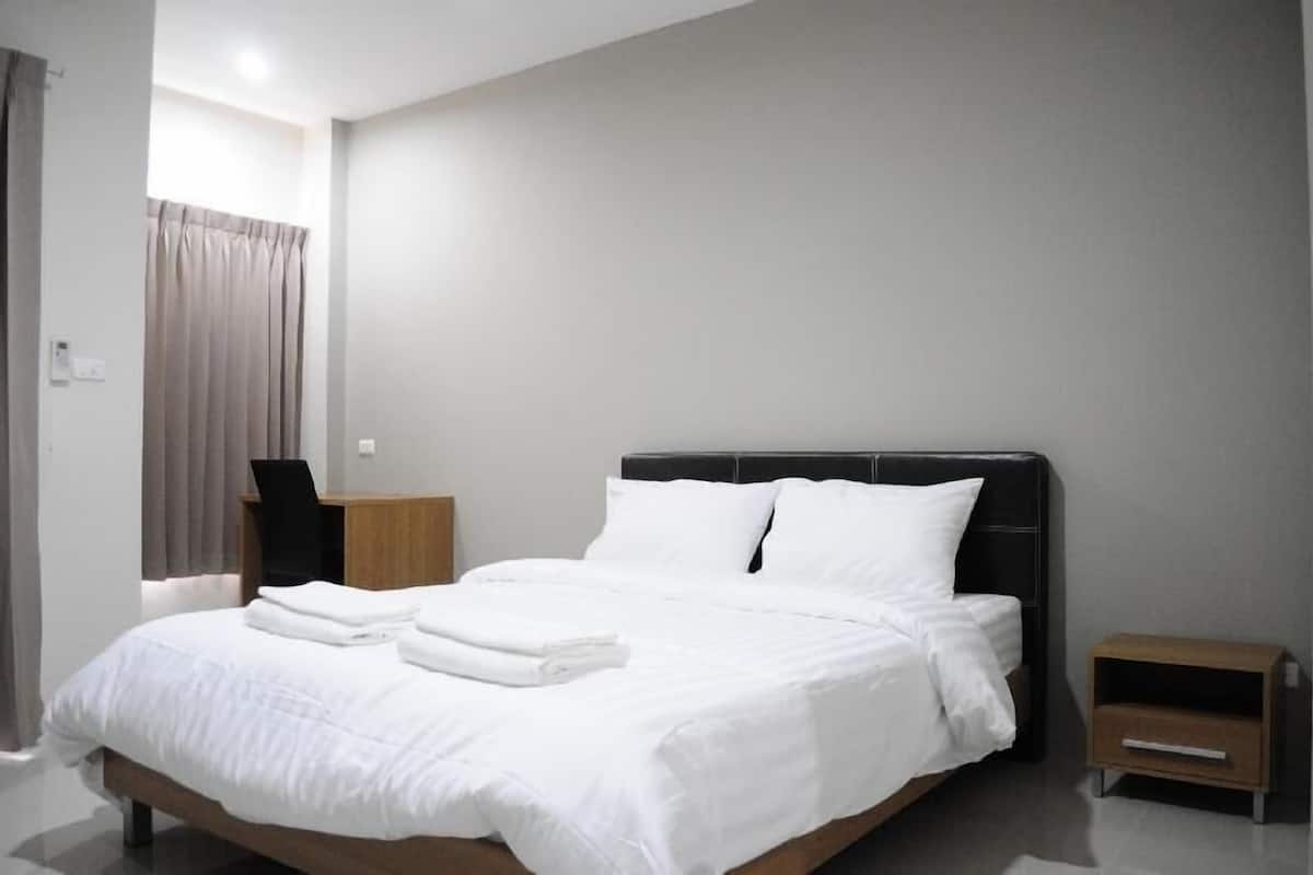 A modern hotel room with a large bed, a wooden nightstand, and a small bedside table.