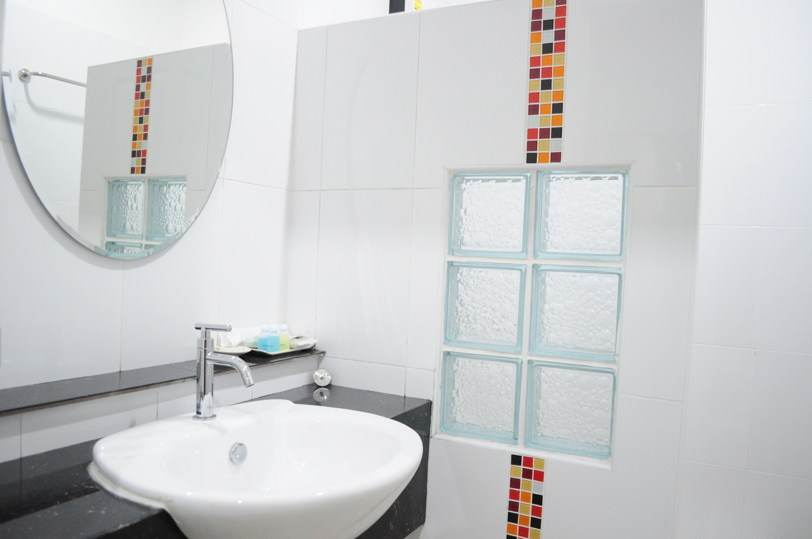 A bathroom with a white sink, a mirror, and a tiled wall with a colorful vertical strip.