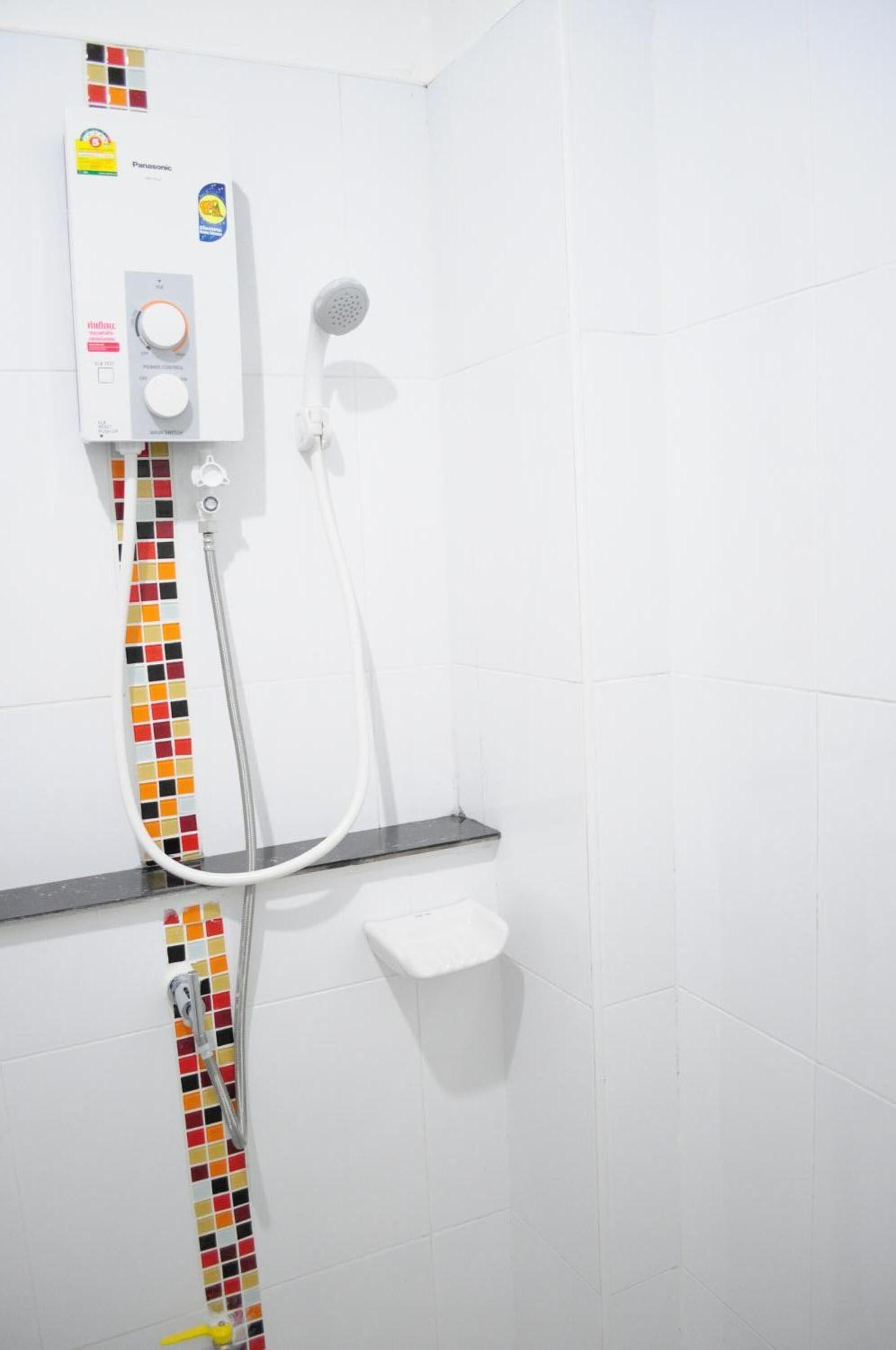 A bathroom with a white tiled wall, a colorful mosaic tile strip, a handheld showerhead, and a control panel.